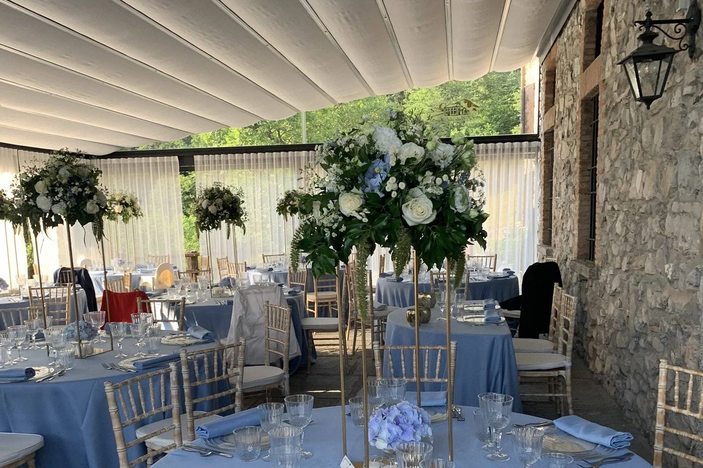 La sala luminosa della location, con tavoli rotondi vestiti di azzurro e sedie Chiavari